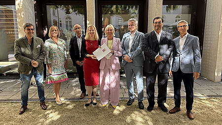 Eine Gruppe von Leuten. Sie halten ein Dokument in der Hand und lächeln.