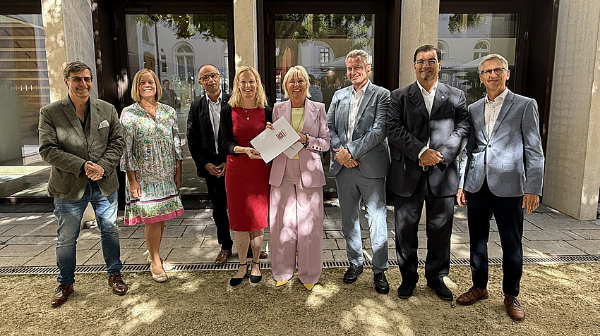 Eine Gruppe von Leuten. Sie halten ein Dokument in der Hand und lächeln.