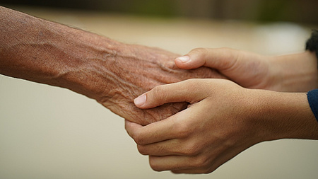 Ein Kind umfasst die Hände einer alten Person