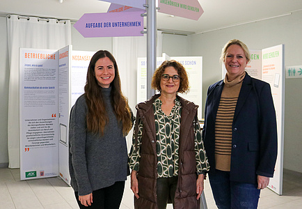 Die drei Frauen stehen vor einem Wegweiser, der Teil der Ausstellung ist.