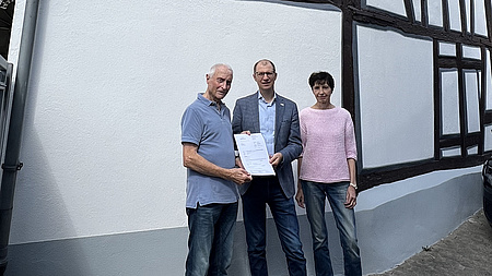 Landrat Jan Weckler und das Ehepaar Berk stehen vor einem frisch sanierten Fachwerkhaus.