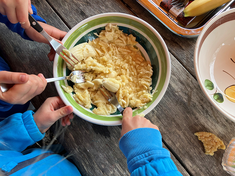 Kinderhände, die Gabeln halten und damit Bananen in einer Schüssel zermatschen.