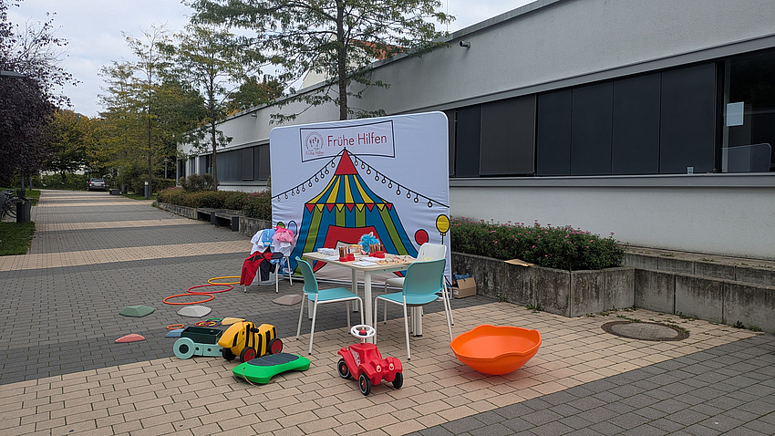 Hier ist ein Stand mit Tisch und vielen Spielmöglichkeiten und Fahrzeugen für Kinder zu sehen
