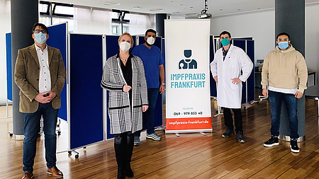 Personengruppe vor einem Aufsteller der Impfpraxis Frankfurt