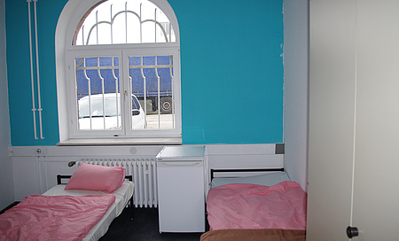 Symbolbild. Zwei Betten stehen durch einen Kühlschrank getrennt nebeneinander. Rechts ein Schrank. Im Hintergrund ein Fenster.