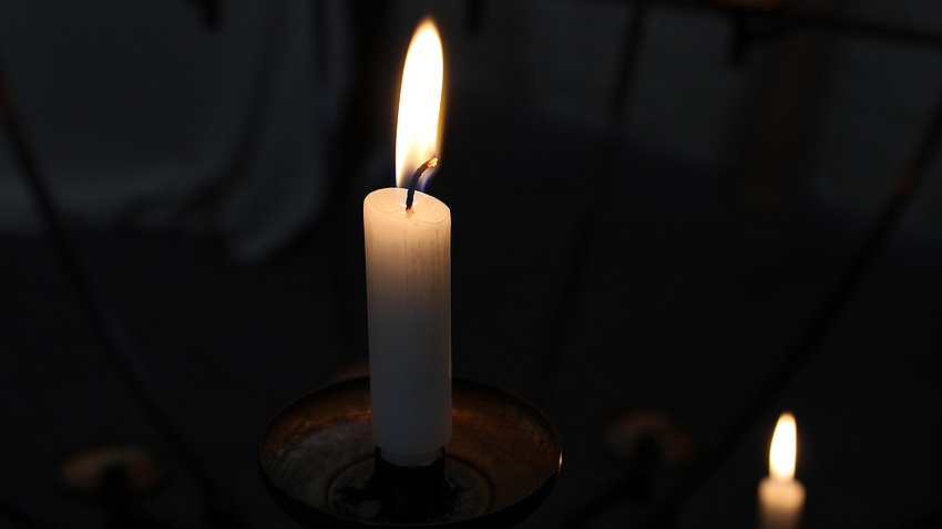 Eine leuchtende Kerze vor schwarzem Hintergrund.