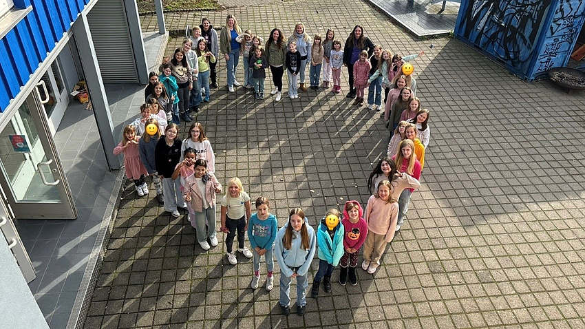 Viele Mädchen stehen in der Form eines Herzens und gucken nach oben in die Kamera
