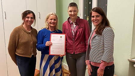 Kreisbeigeordnete Marion Götz, Dr. Marina Gebbers, Ute Latzel und Miriam Hock präsentieren ein Dokument und lächeln in die Kamera.