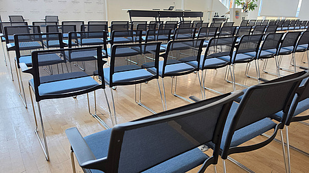 In einem großen Saal stehen mehrere Reihen unbesetzter Stühle.