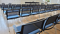 In einem großen Saal stehen mehrere Reihen unbesetzter Stühle.