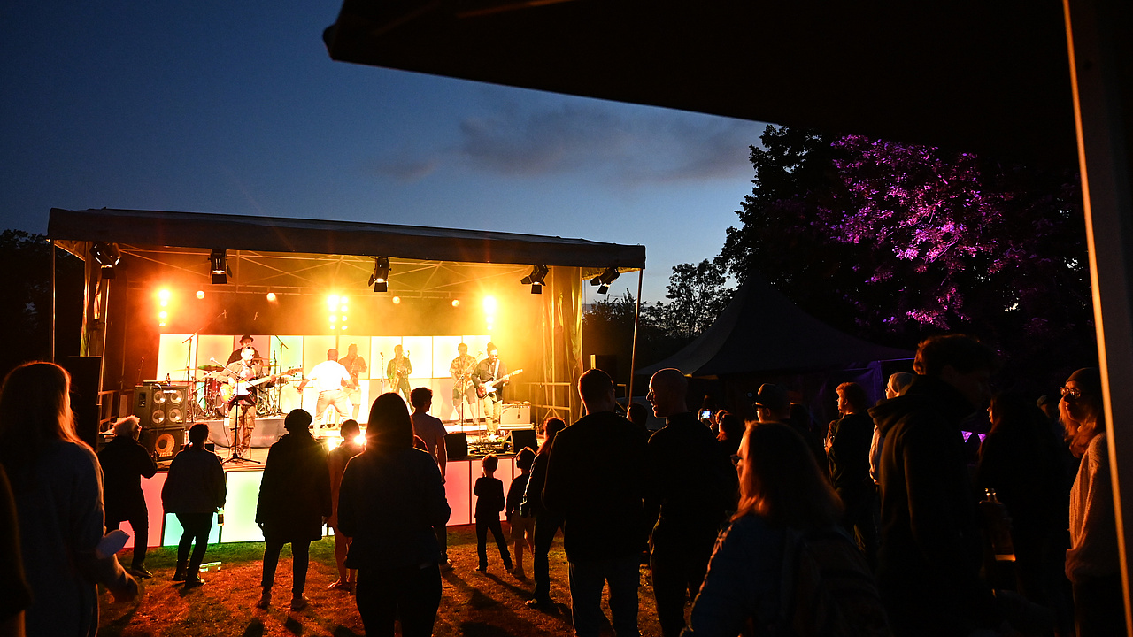 Eine Gruppe von Menschen steht vor der Bühne  auf der eine Band musiziert.