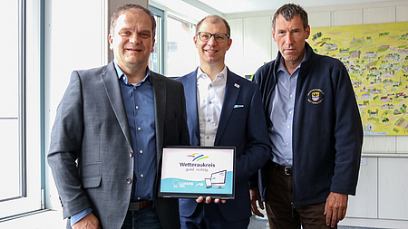 Drei Männer zeigen eine App auf einem iPad.