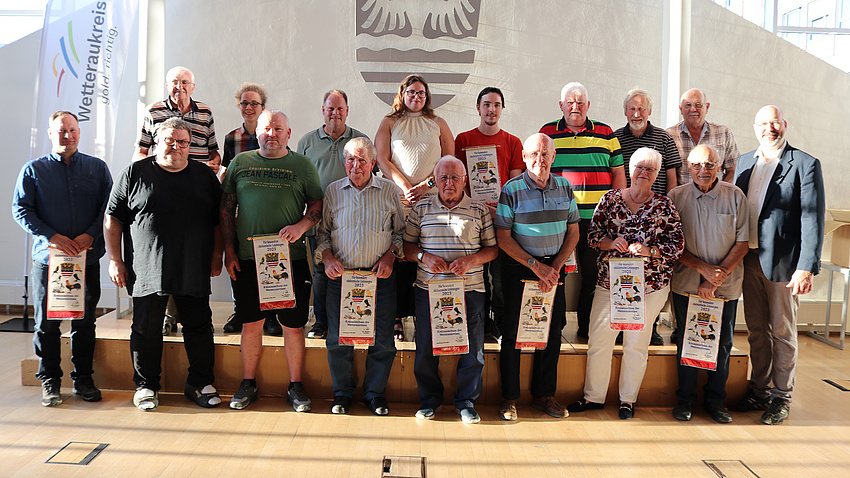 Viele Menschen stehen in einem Saal und halten Urkunden in den Händen.