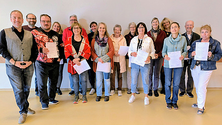 Eine größere Gruppe aus Frauen und Männern steht in einem größeren Raum. Einige von ihnen halten Urkunden in Händen.