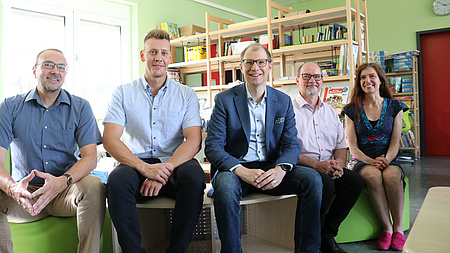 Fünf Erwachsene sitzen in einer Leseecke für Kinder in einem Klassenzimmer.