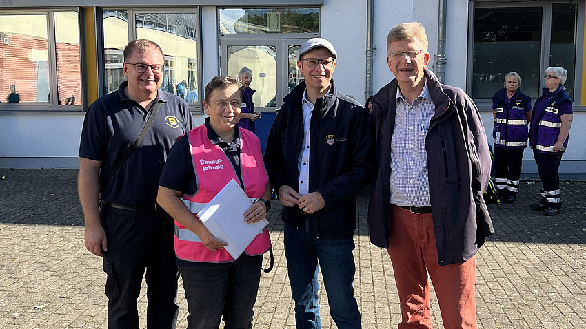 Landrat Jan Weckler, Pfarrerin Christine Zahradnik, Fachdienstleiter Jürgen Nickel und Präses Dr. Volkmar Oberklus stehen vor einem Gebäude. Sie lächeln in die Kamera.