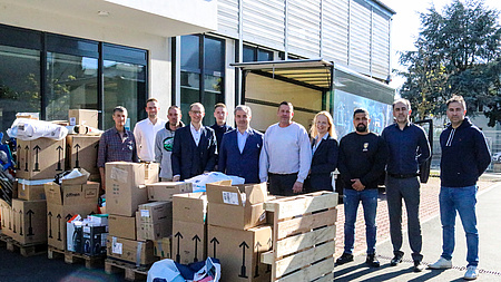 Elf Männer und Frauen vor einem Gebäude. Vor ihnen stehen viele gefüllte Umzugskartons.