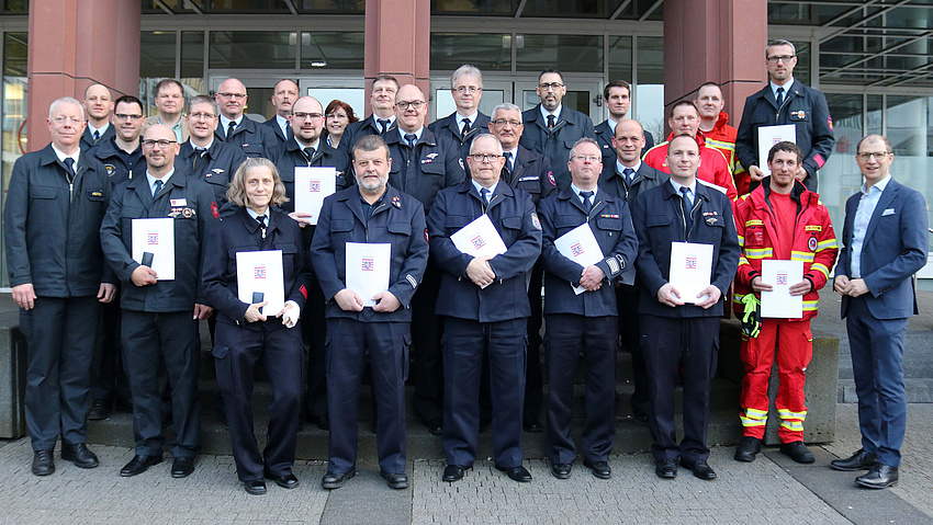 23 Männer und Frauen in dunkelblauer Uniform präsentieren stolz ihre Urkunde.