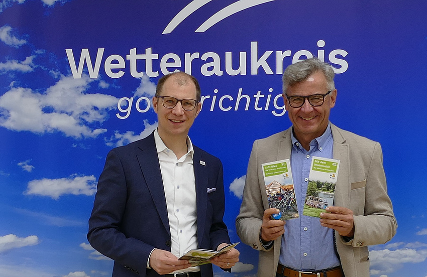 Zwei Männer halten Broschüren in der Hand. Im Hintergrund der Schriftzug: Wetteraukreis. Gold richtig