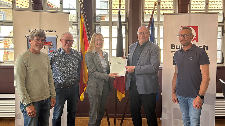 Vier Männer und eine Frau lächeln in die Kamera. Sie halten ein Dokument in der Hand.