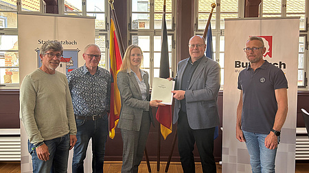 Vier Männer und eine Frau lächeln in die Kamera. Sie halten ein Dokument in der Hand.