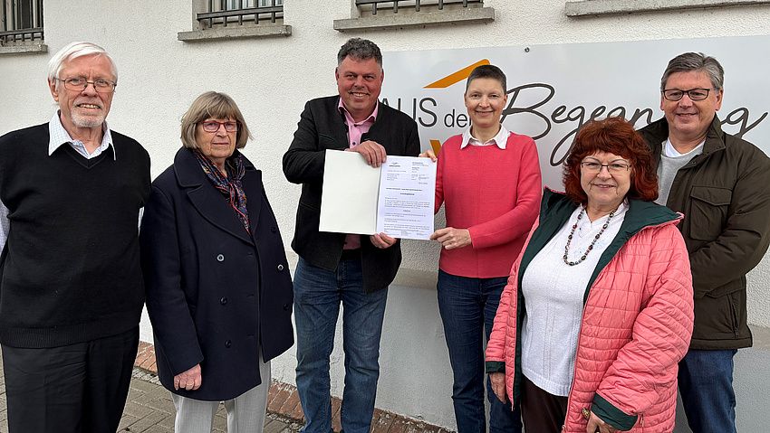 Sechs Leute vor einem Gebäude, an dem ein Schild "Haus der Begegnung" hängt.