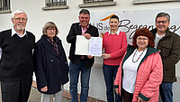 Sechs Leute vor einem Gebäude, an dem ein Schild "Haus der Begegnung" hängt.