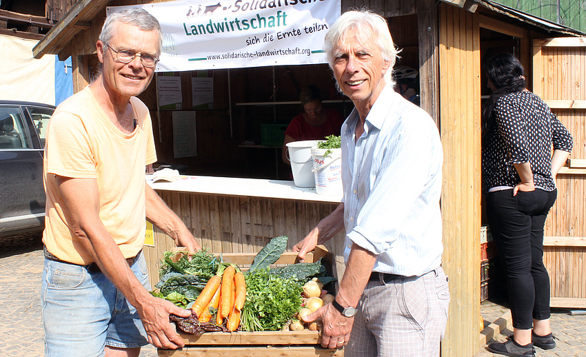 Zwei Männer halten eine Kiste mit frischem Gemüse