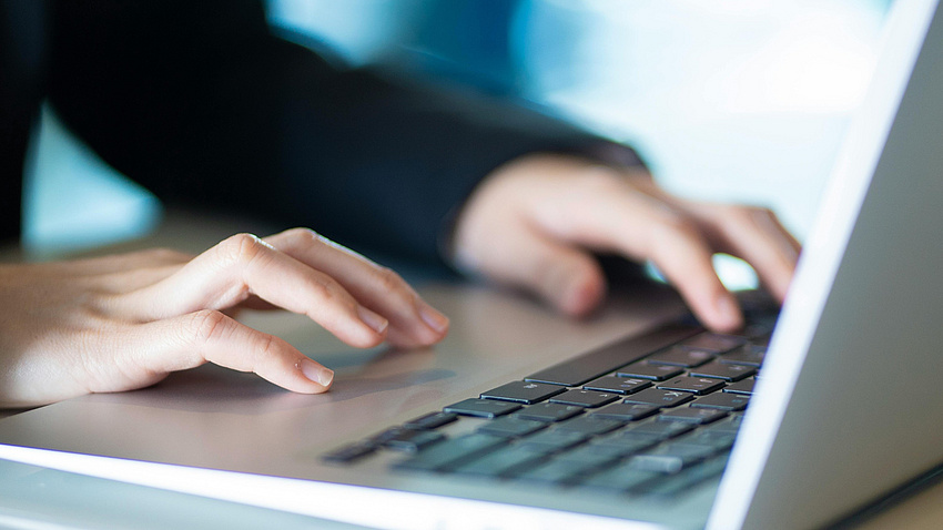 Das Bild zeigt die Hände einer Person, die an einem Laptop arbeitet.