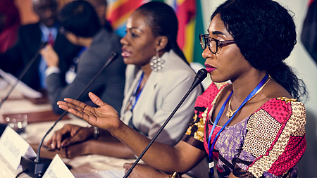 zwei dunkelhäutige Frauen sitzend vor Mikrofonen