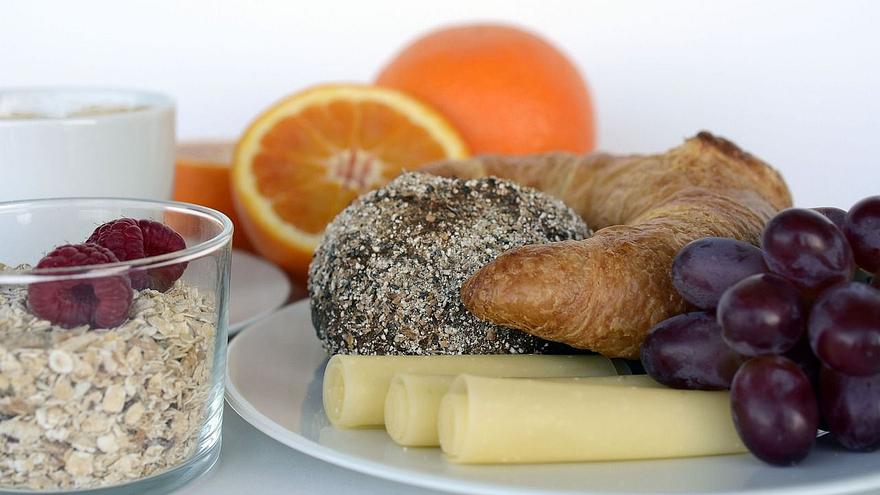 Frühstücksteller mit Käse, Trauben und Croissant sowie ein Müsli mit Obst