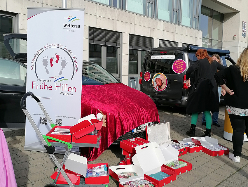 Mangels Tischfläche stehen die roten Köfferchen mit Informationsmaterial auf dem Gehwegpflaster