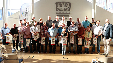 Viele Menschen stehen in einem Saal und halten Urkunden in den Händen.