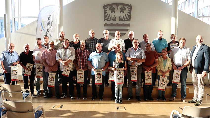 Viele Menschen stehen in einem Saal und halten Urkunden in den Händen.