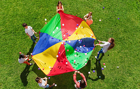 Kinder verschiedener Nationalitäten auf einer grünen Wiese spannen gemeinsam ein buntes Tuch