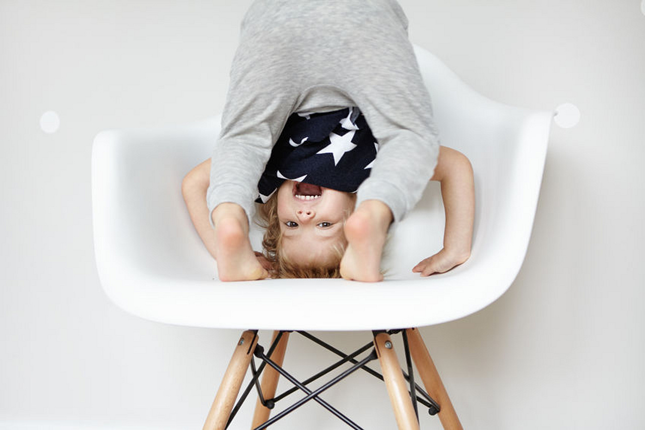 Kind steht kopfüber auf einem Stuhl