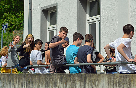 Junge Menschen sitzen auf einem Geländer. Einige von ihnen haben sich umgedreht und zeigen den Daumen nach oben.