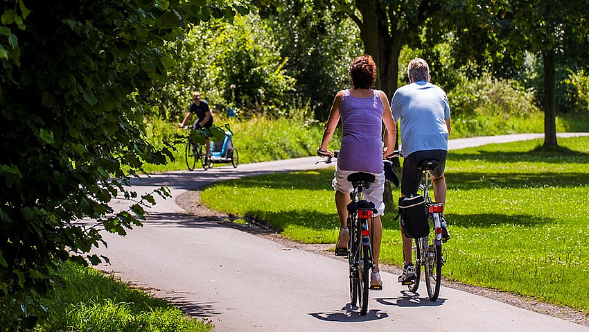 Eine Frau und ein Mann radeln mit dem Fahrrad durch einen Park