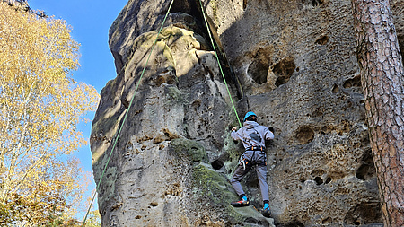 . Ein Junge klettert am Felsen entlang, während ein anderer ihn absichert.