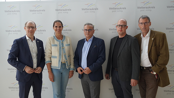 Fünf Personen stehen anlässlich der Infoveranstaltung vor einer Wand mit der Aufschrift Wetteraukreis und des Logos.