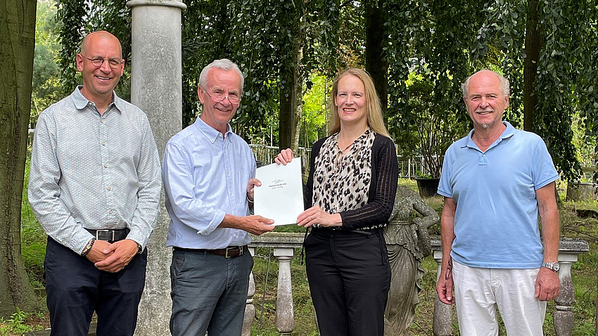 Drei Männer und eine Frau halten ein Dokument in die Kamera.