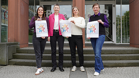 Vier Frauen halten ein Plakat in die Kamera.