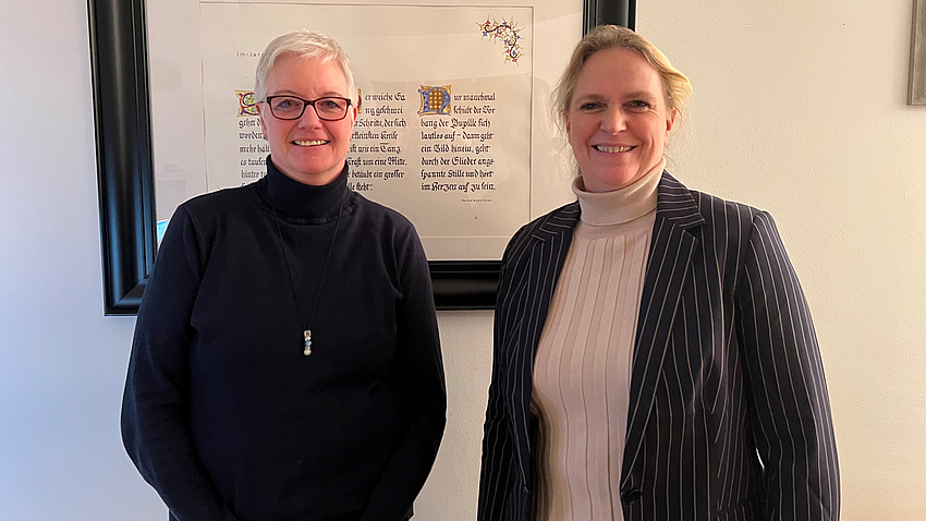 Zwei Frauen stehen nebeneinander und lächeln in die Kamera.