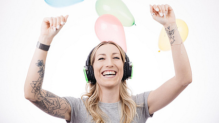 Ein junge Frau tanzt mit Kopfhörer auf den Ohren, die Arme hält sie oben