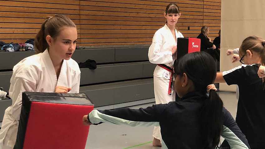 Junge Mädchen absolvieren in einer Sporthalle Übungen einer asiatischen Kampfsportart.