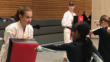 Junge Mädchen absolvieren in einer Sporthalle Übungen einer asiatischen Kampfsportart.