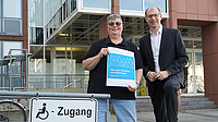 Zwie Menschen stehen an einem Schild, das den barrierefreien Zugang ausschildert.