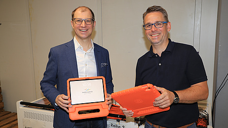 Zwei Männer stehen in einem Raum und beide halten je ein Tablet in der Hand.