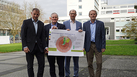 Vier Männer stehen nebeneinander und präsentieren ein Plakat mit der Aufschrift "Wachstumsmotor Wetterau"