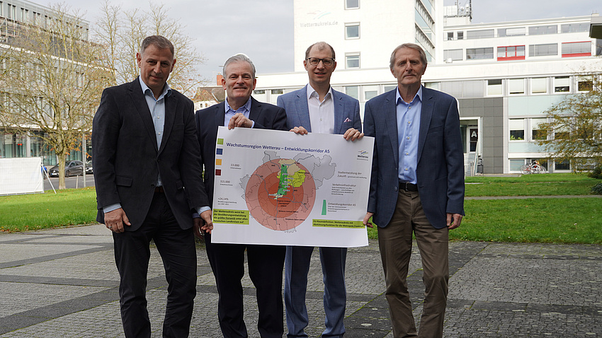 Vier Männer stehen nebeneinander und präsentieren ein Plakat mit der Aufschrift "Wachstumsmotor Wetterau"